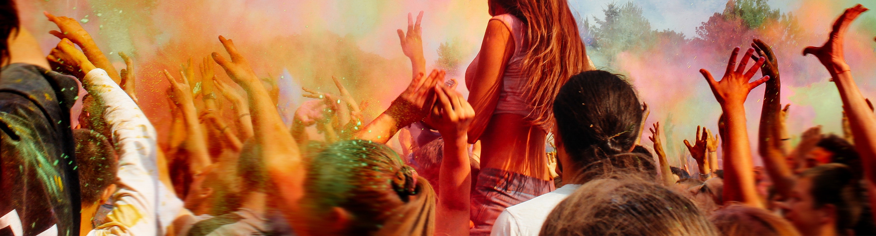A crowd of the people with their hands in the air throwing colourful powder for Holi Festival