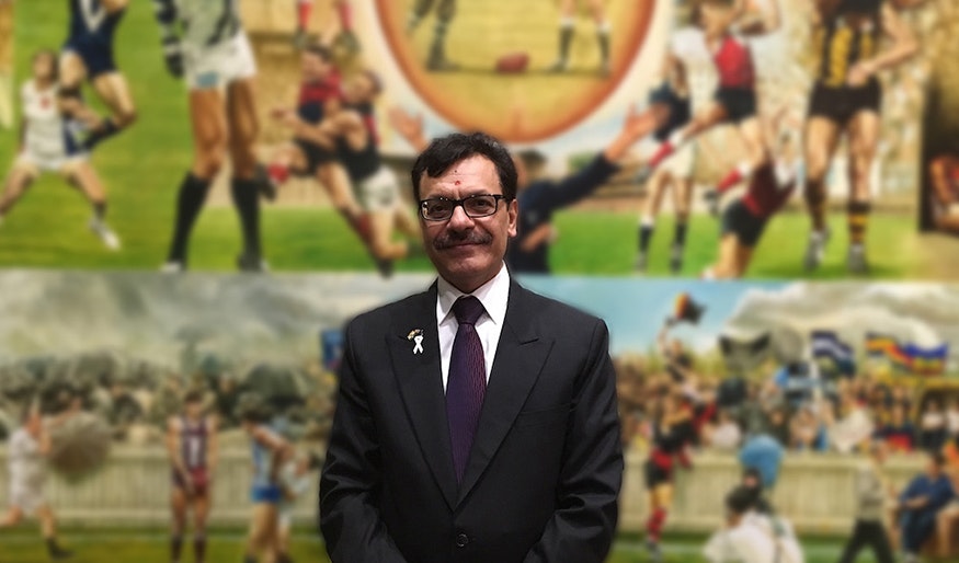 A photo of Arun standing in front of a collage of AFL paintings