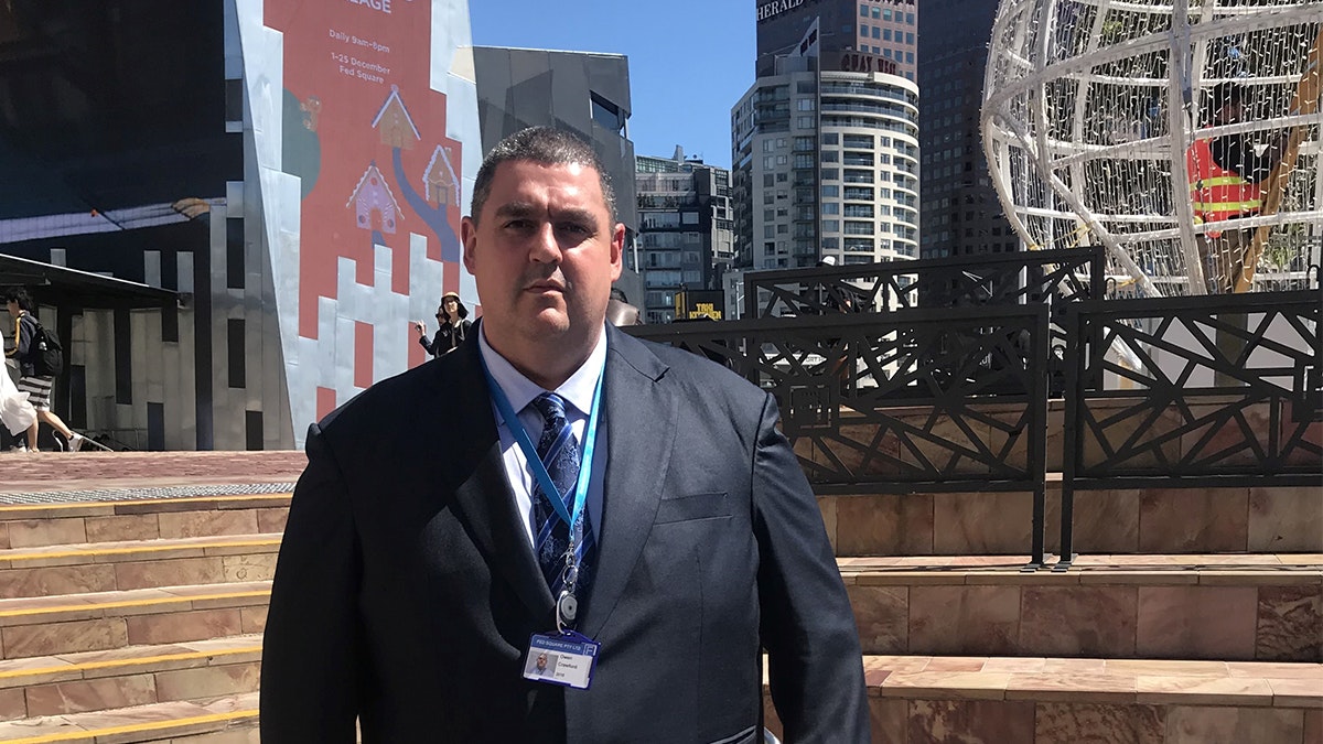 Owen Crawford is standing near the stairs up to the main square at Fed Square and he is wearing a suit and tie