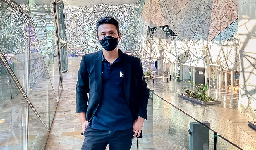 Suranjan is standing on the balcony inside The Atrium at Fed Square wearing a black suit