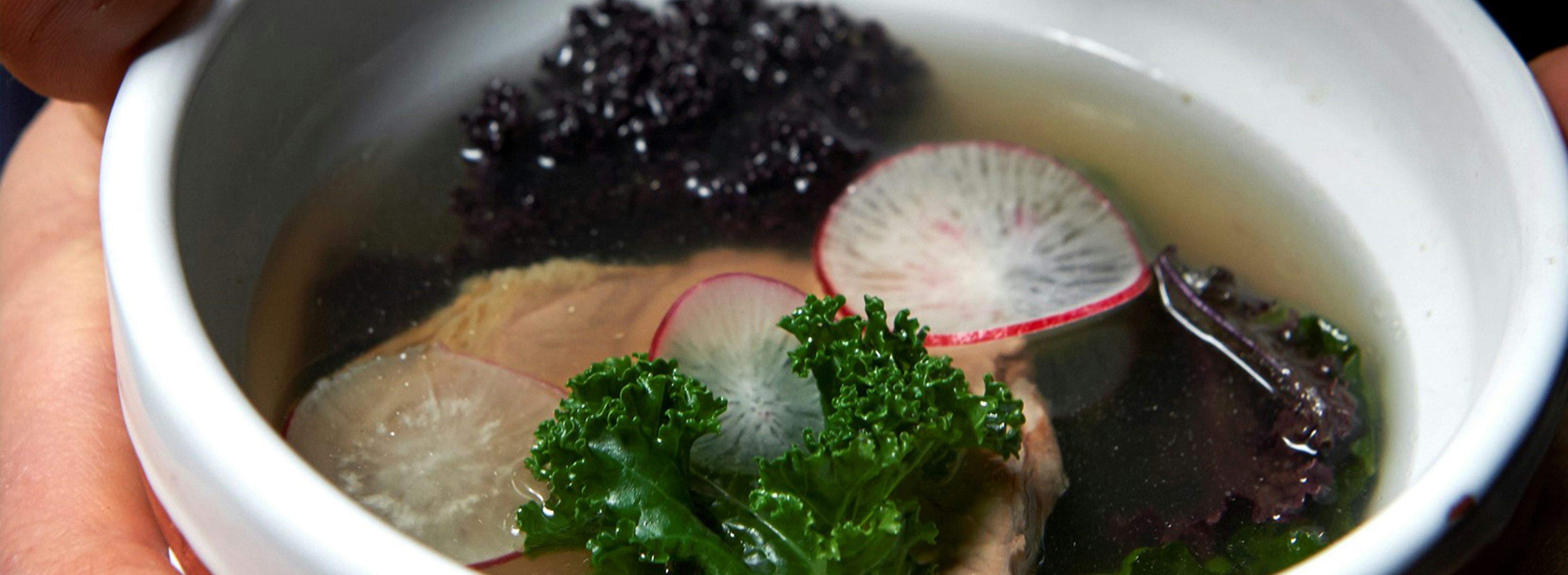 A close up photo of a light broth with vegetables in a white bowl