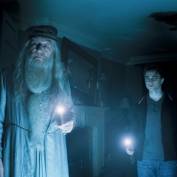 Dumbledore and Harry are in a dark room holding their wands with the tips lit in the Half Blood Prince