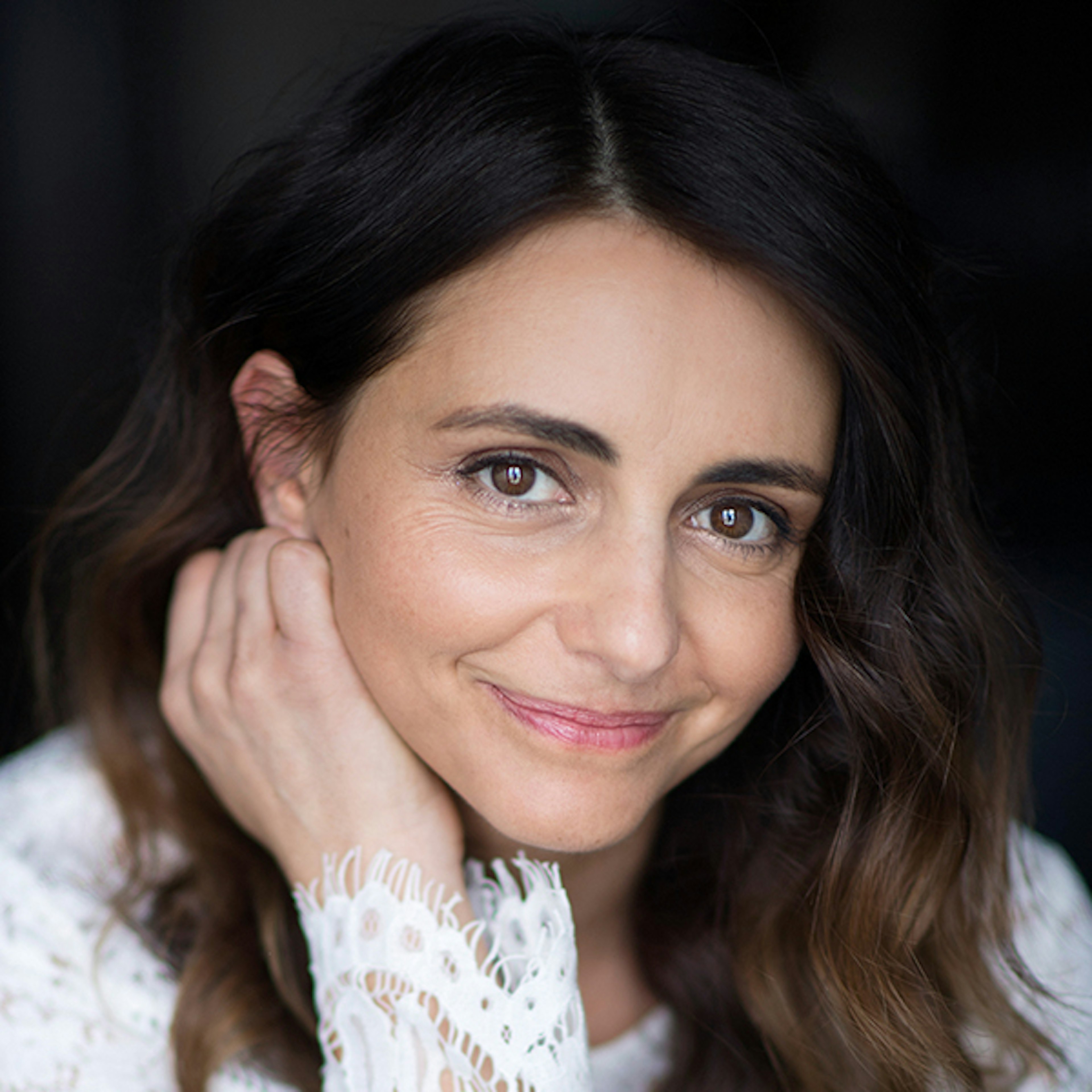 A headshot of Pia Miranda smiling with her hand resting on the right side of her face