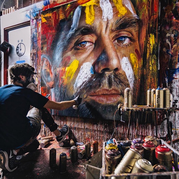 Street artist Adnate is spray painting an artwork of Adam Goodes