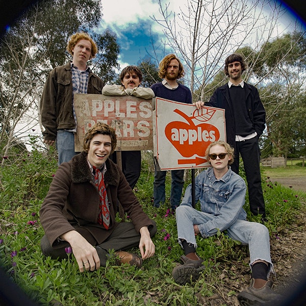 The six members of Bones and Jones are posing together in front of some apple's signs on a country road