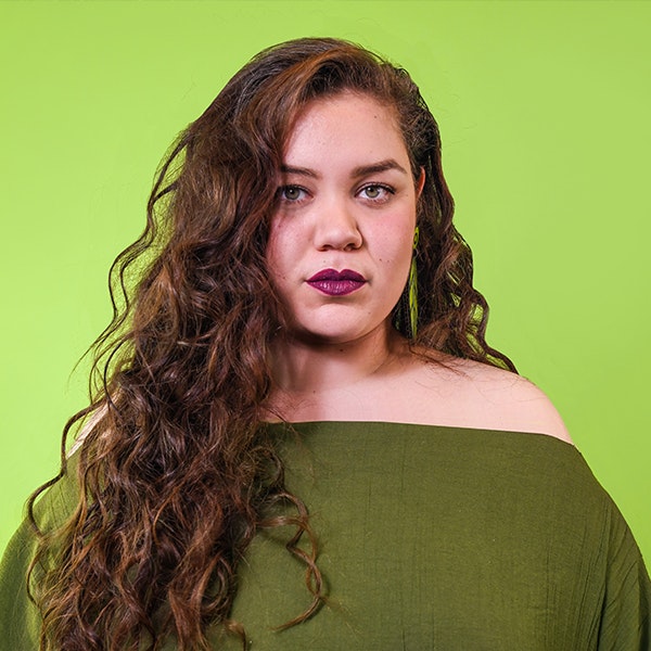 Musical artist Bumpy is looking at the camera wearing an olive green shirt in front of a light green background