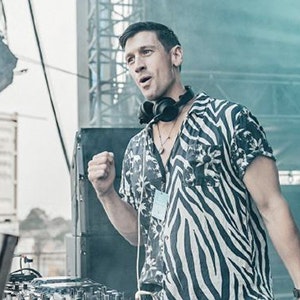 DJ Any Murphy is wearing a zebra print shirt on stage with headphones around his neck