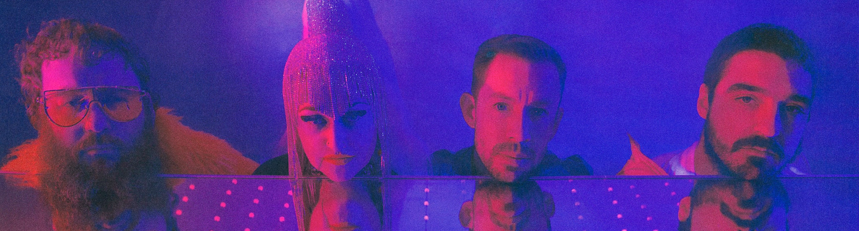 The four members of Hiatus Kaiyote are looking at the camera with the heads resting above a mirror under blue and pink light