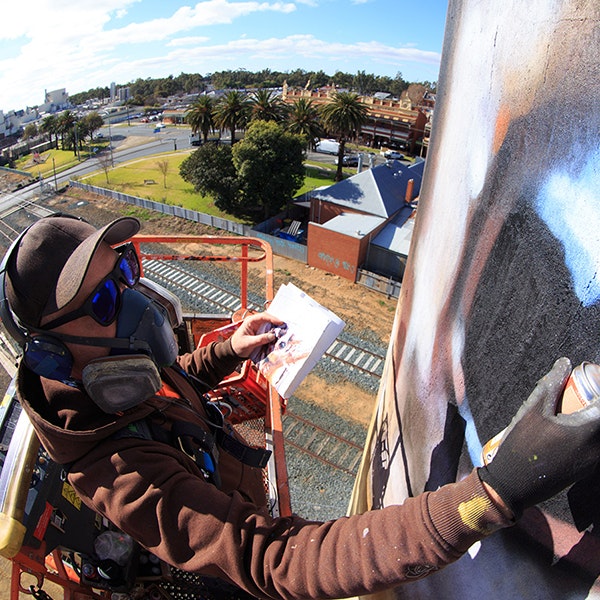 Silo artist Jimmy Dvate is up on a scissor lift spray painting a silo