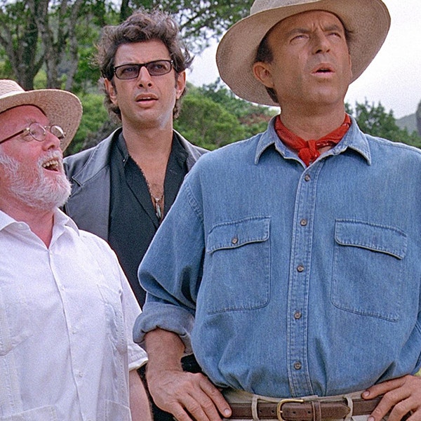 Sam Neil, Richard Attenborough and Jeff Goldblum are looking at a dinosaur off camera in Jurassic Park