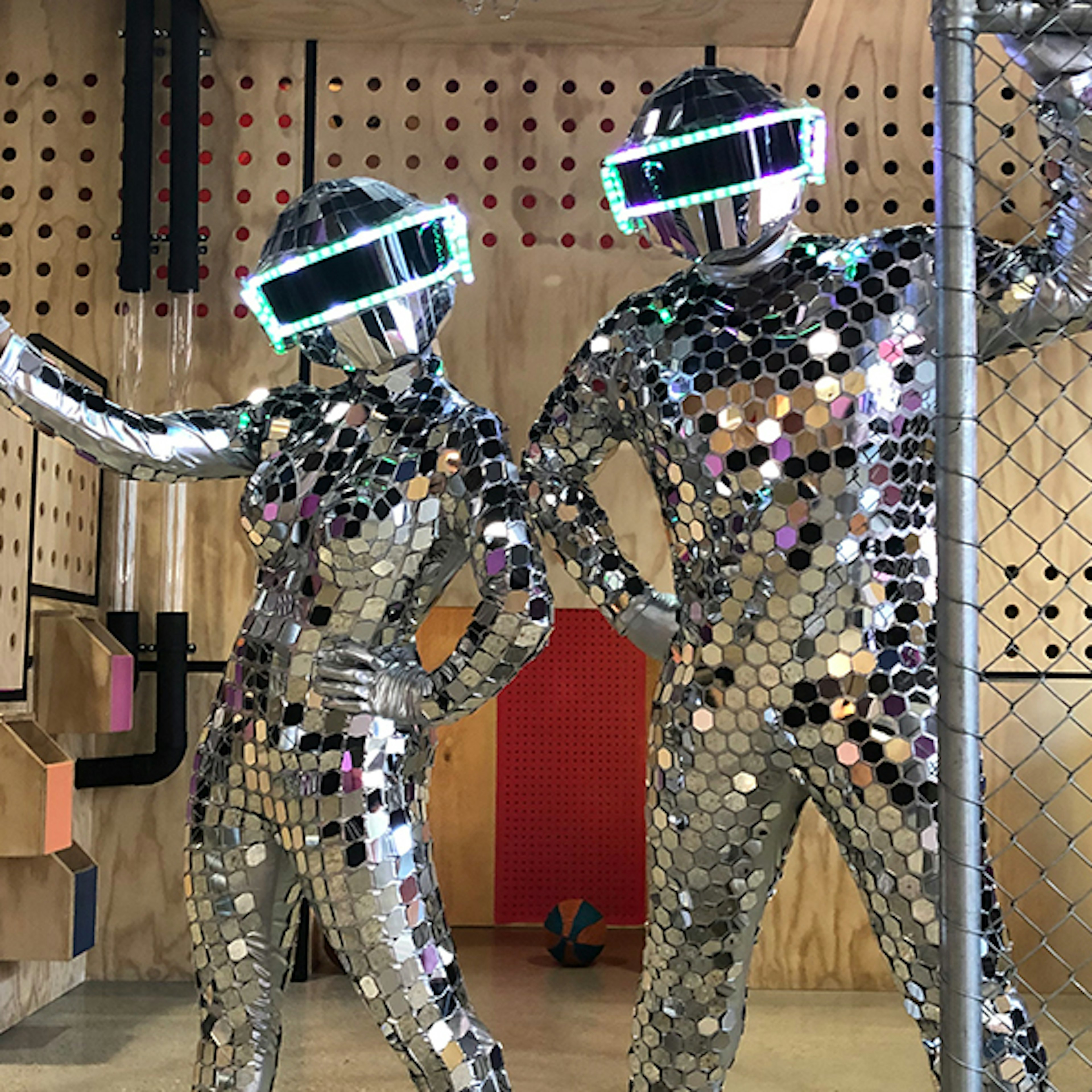 Two Mirror Ball Dancers standing side by side holding onto a fence