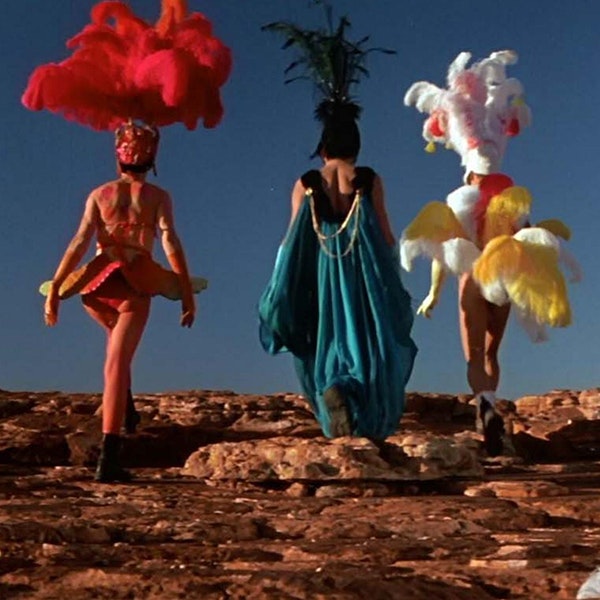 The three drag queens are dressed in their costumes walking away from the camera in Priscilla Queen of the Desert