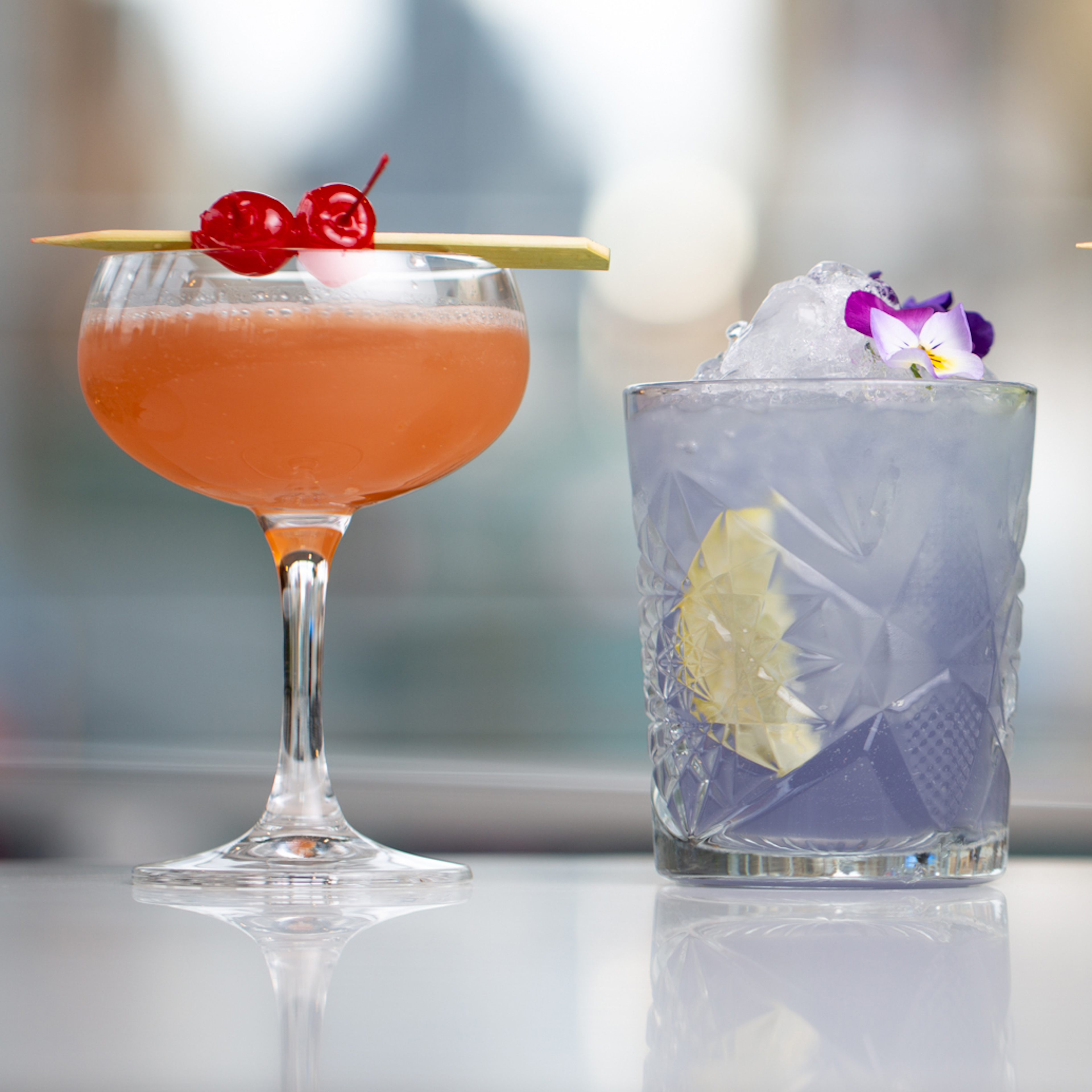 An image of an orange cocktail on the left and a purple cocktail on the right