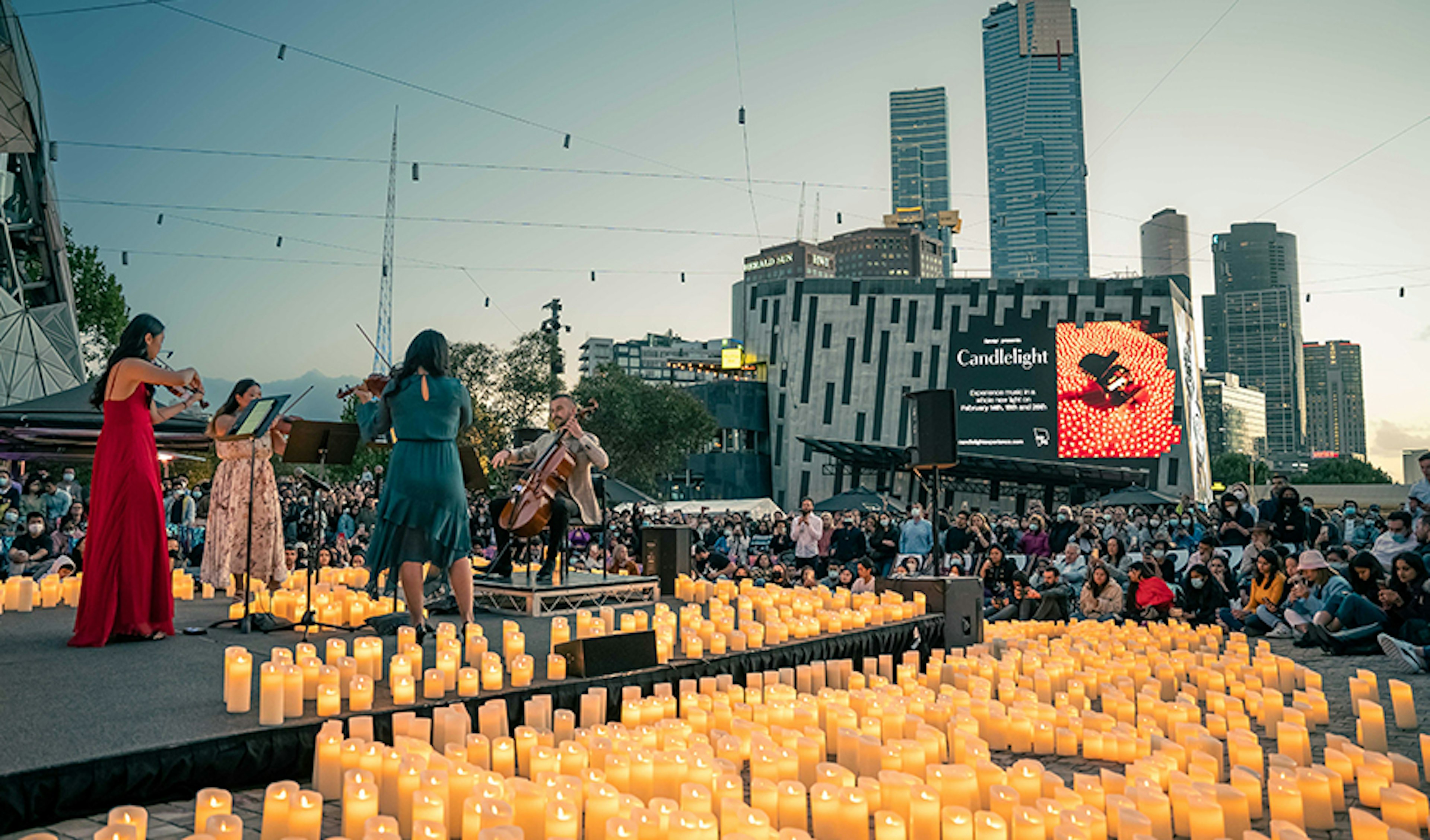 A string quartet playing in the middle of Fed Square surrounded by candles at dusk