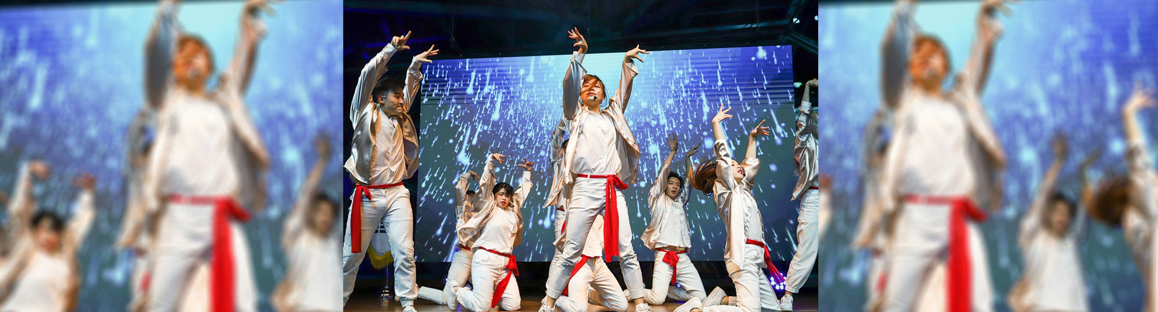 A group of people dancing on stage at the K-Pop World Festival in Melbourne, they are wearing white clothes with a red sash around their waists while mid dance pose