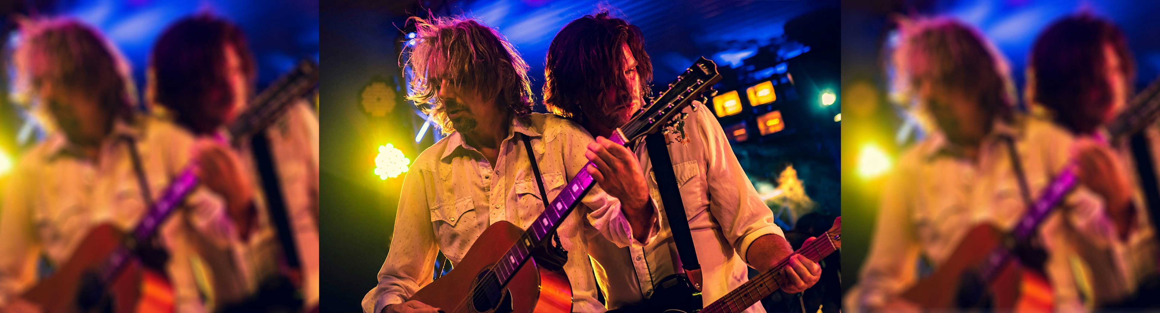 Tex Perkins is standing directly behind Matt Walker on stage while they both play guitar