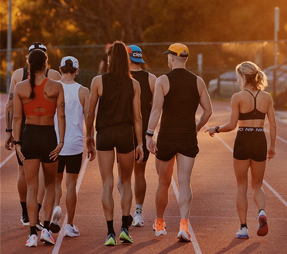A group of people in fitness clothing are walking in a group with their backs to the camera on a running track