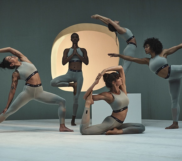 A group of woman all wearing the same grey fitness clothing doing a range of yoga poses on a set