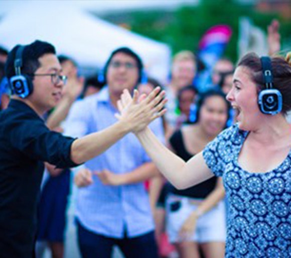 Two happy people wearing headphones at a silent disco and hi fiving while smiling
