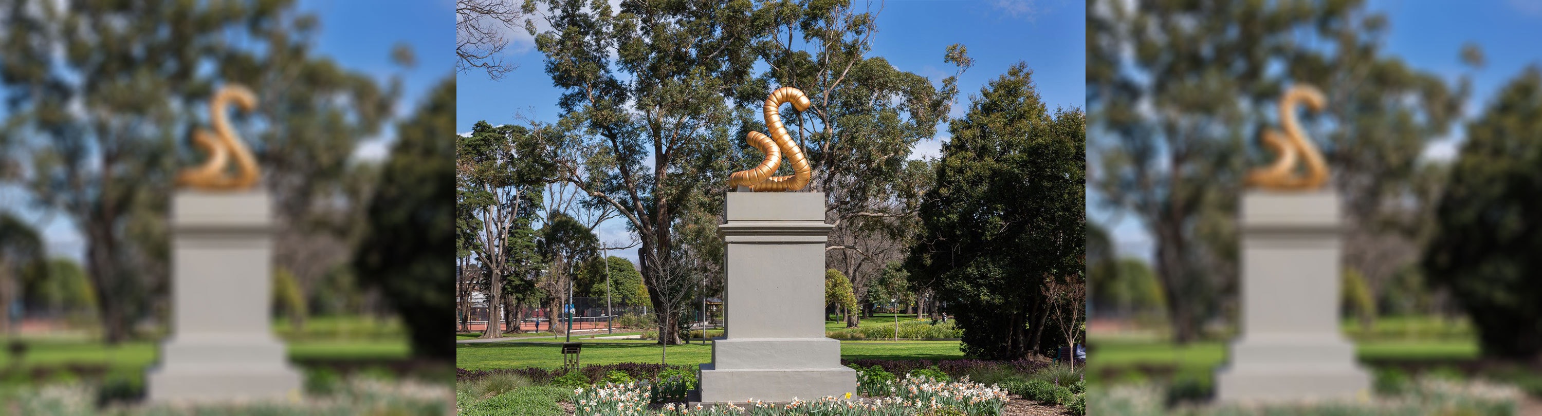 A sculpture of a golden worm that is curled sitting on top of a grey stone plinth