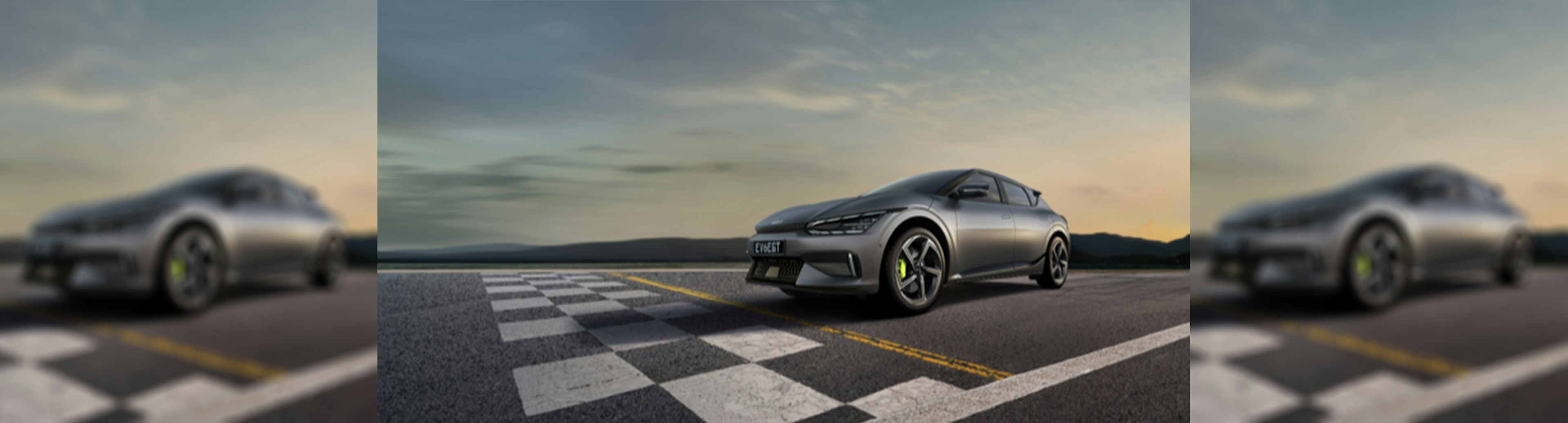 A grey KIA EV6 hatchback at a checkered start line with some hills in the background