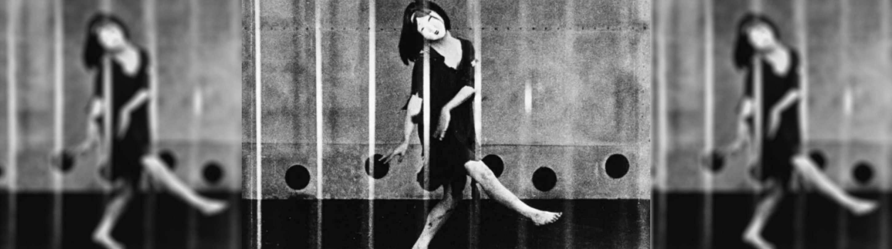 A black and white photo of a woman dancing on stage wearing a Japanese still mask