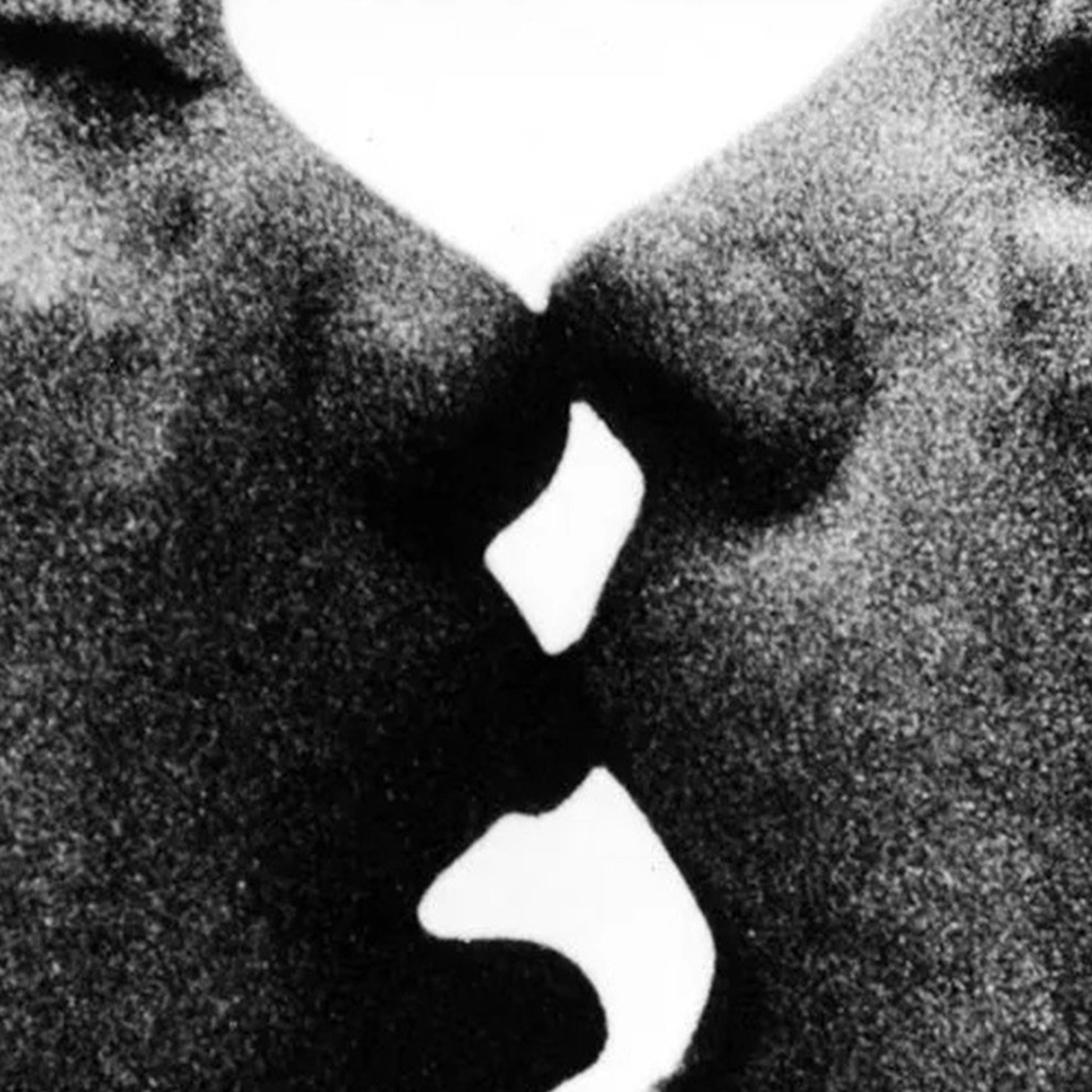 A grainy black and white photo of a close up of two women kissing. The photo focuses on their mouth and nose