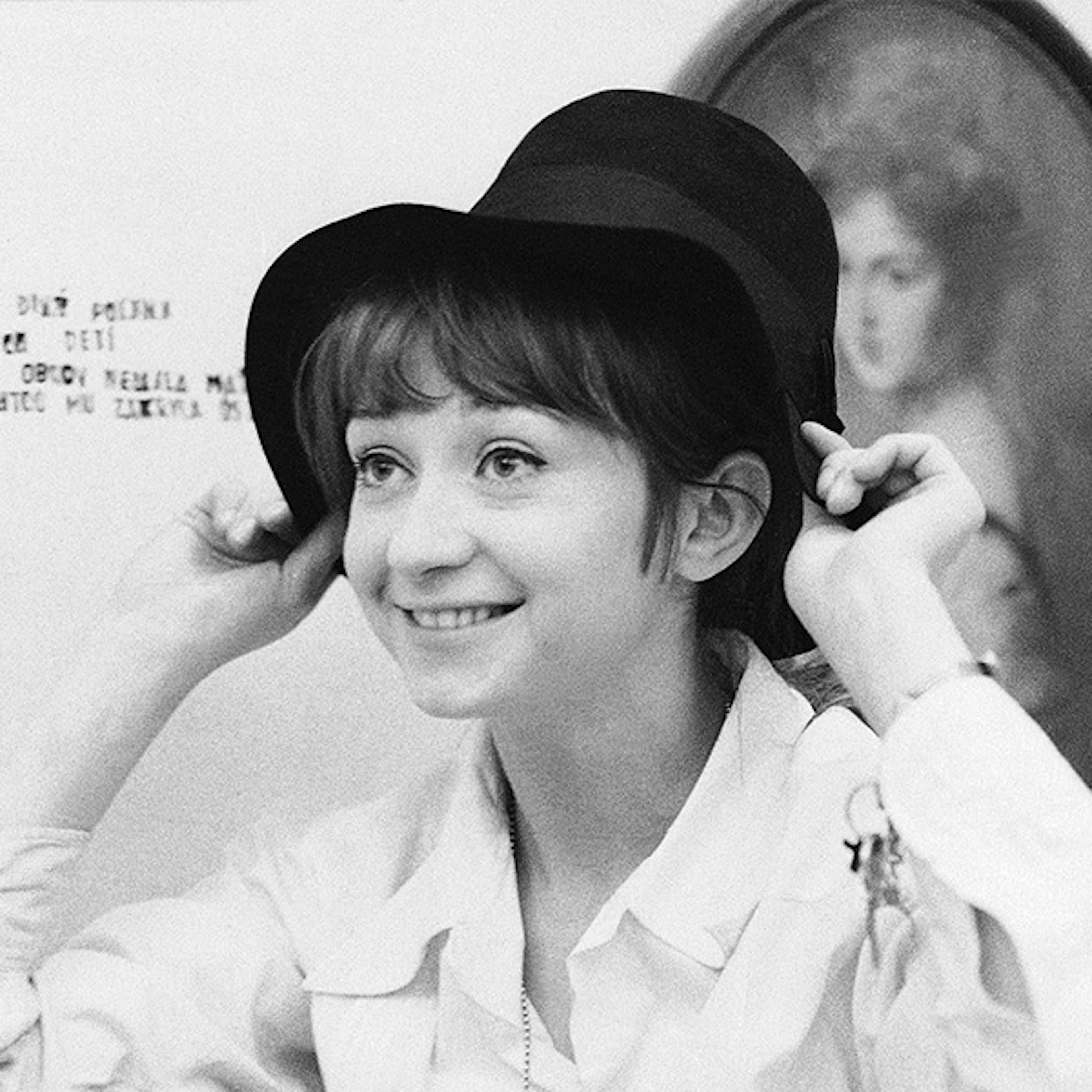 A black and white photo of a woman putting on a hat with a brim, she is not looking into the camera