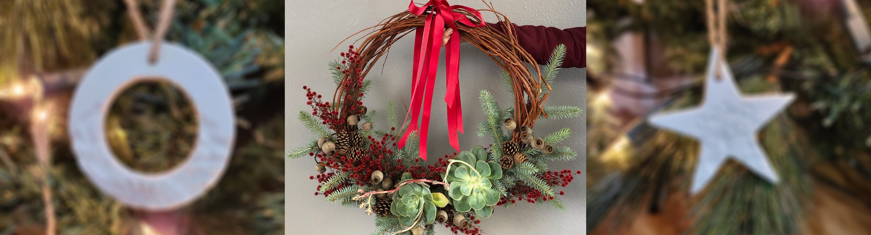 An image of a festive season wreath with a red ribbon draping down from the top and a hand from the right of the image is holding the wreath