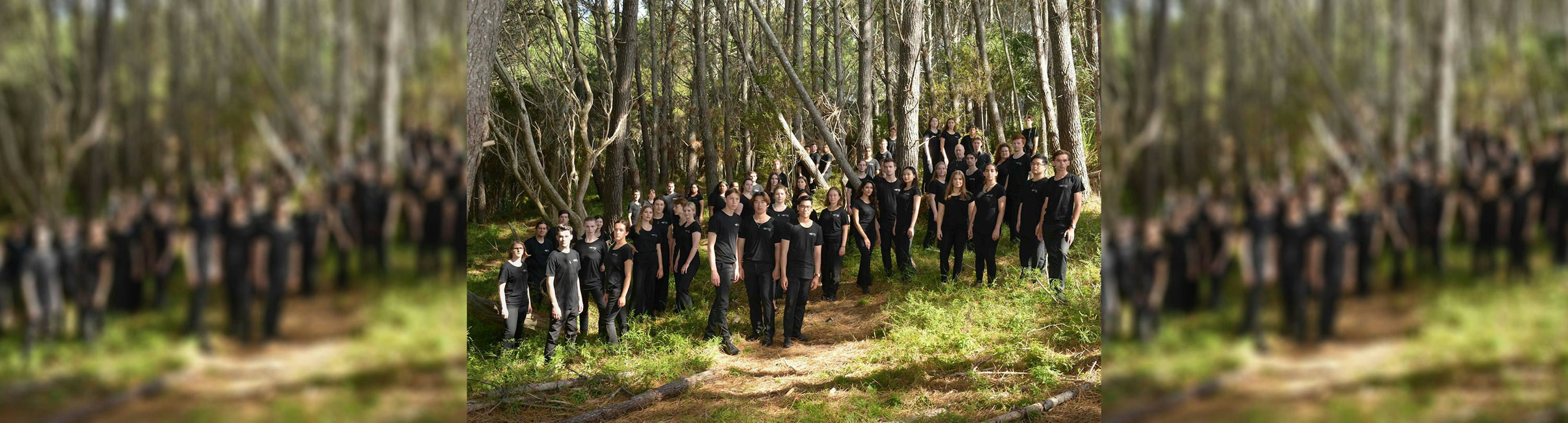 A group of about 30 teenagers for the New Zealand Youth Choir all wearing black and standing in a forest