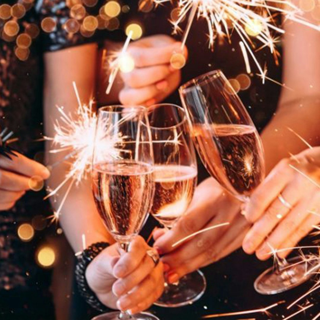 Three people out of view each holding a champagne flute and a sparkler doing a cheers