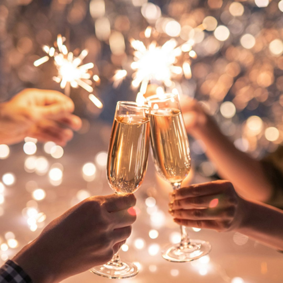Two champagne flute cheersing as sparklers are light behind them