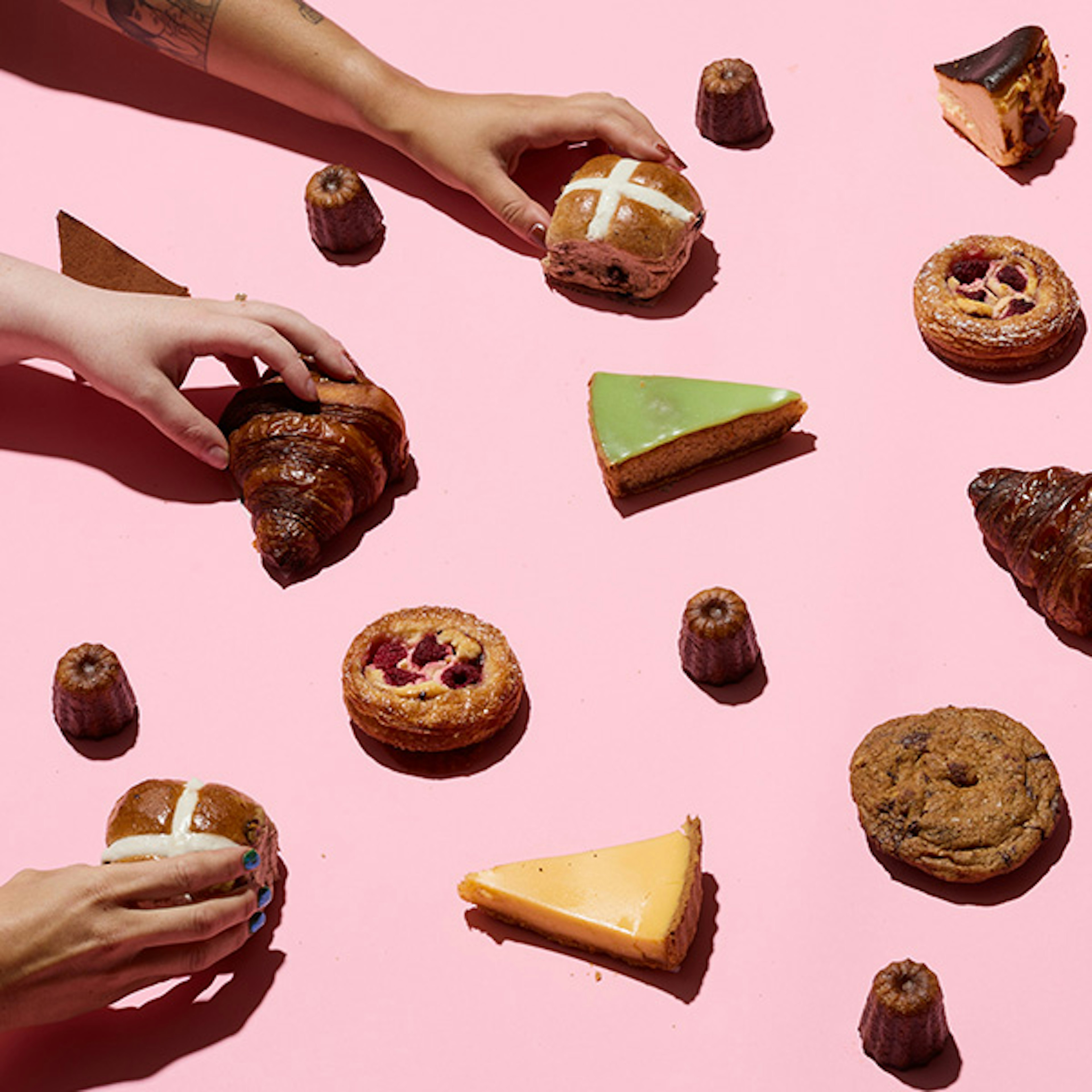 Lots if different pastries sitting on a light pink background with three hands coming in from the left grabbing three different items