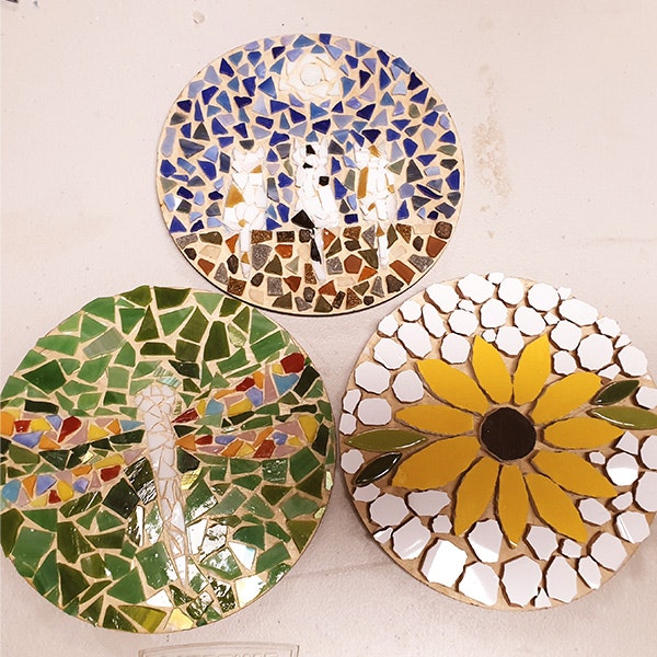Three small circular mosaics. The bottom left circle is green with a white dragonfly, the bottom right is a yellow sunflower surrounded by white tiles, and the top circle is the cats sitting on a wall