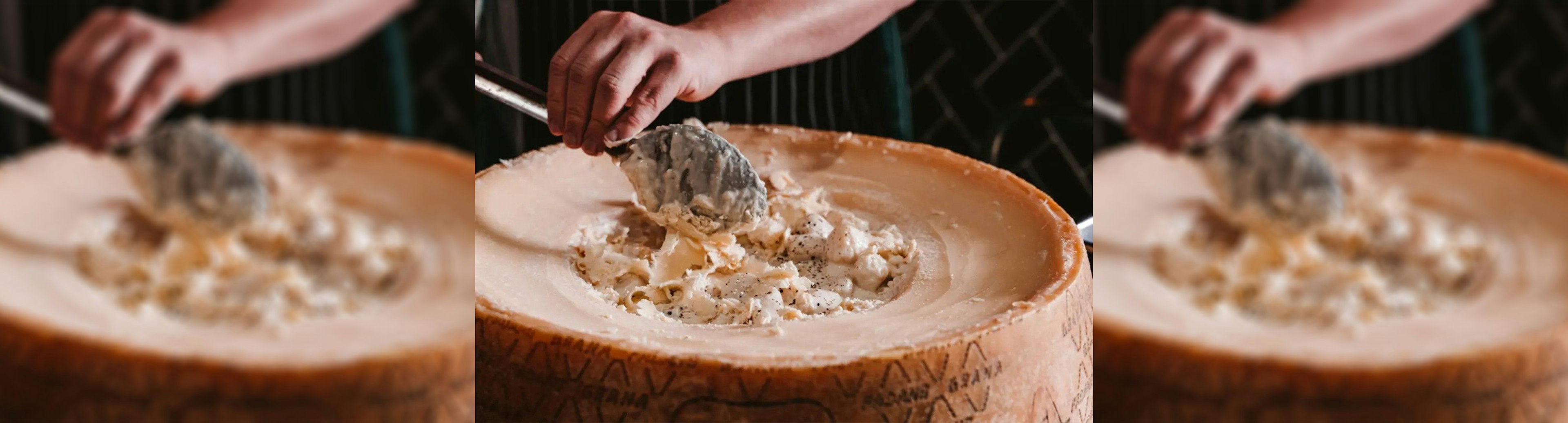 A close up of a big wheel of cheese with a person scooping out the inside with a spoon