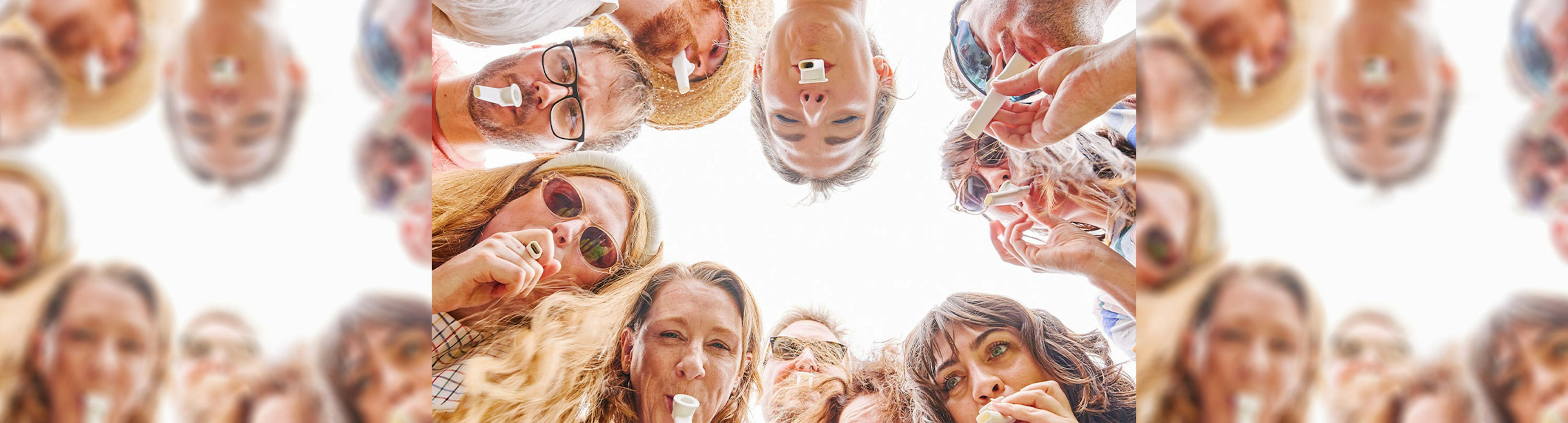 A group of people in a circle looking down at the camera with kazoos in their mouths