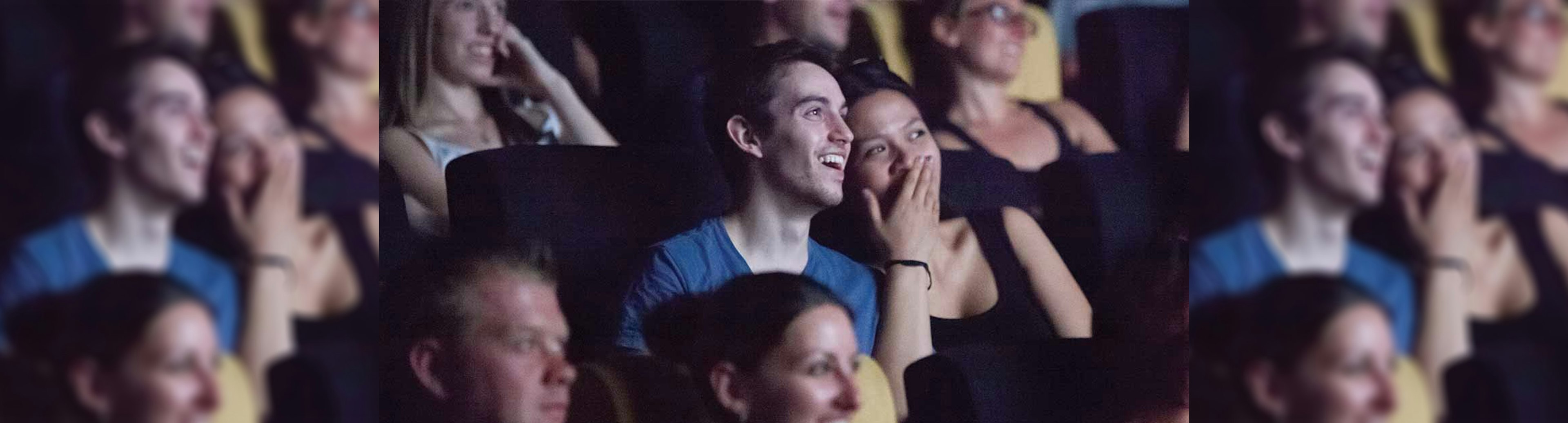 A couple sitting next to each other in a theatre looking at the stage and laughing while leaning in close