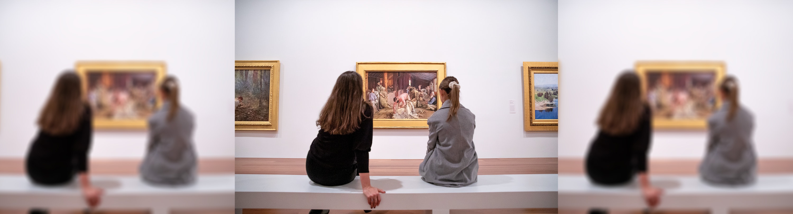 Two women sitting on a white bench in The Ian Potter Centre: NGV Australia looking at a painting of a man shearing
