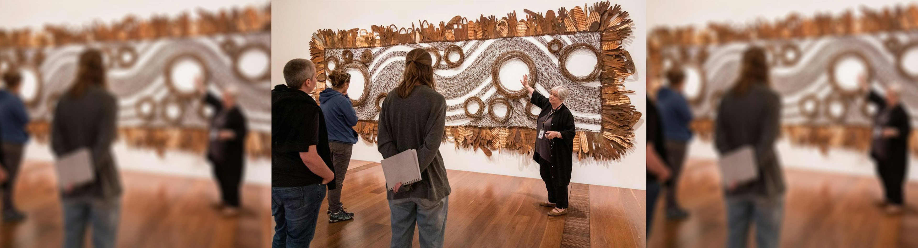 A tour guide is standing in front of an artwork talking to a group of people