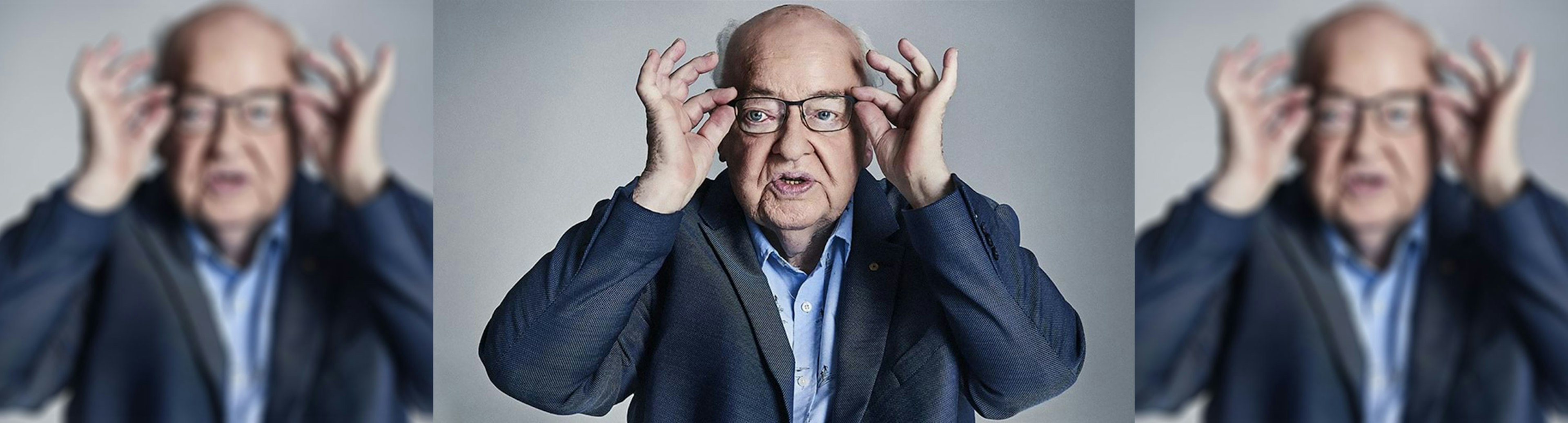 A portrait photo of Father Bob Maguire wearing a blue suit putting his glasses on