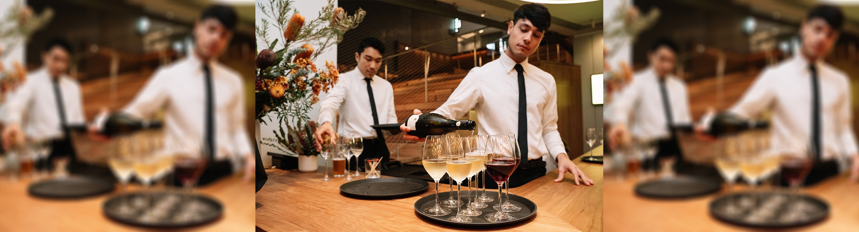 Two waiters pouring wine at the front desk of ACMI