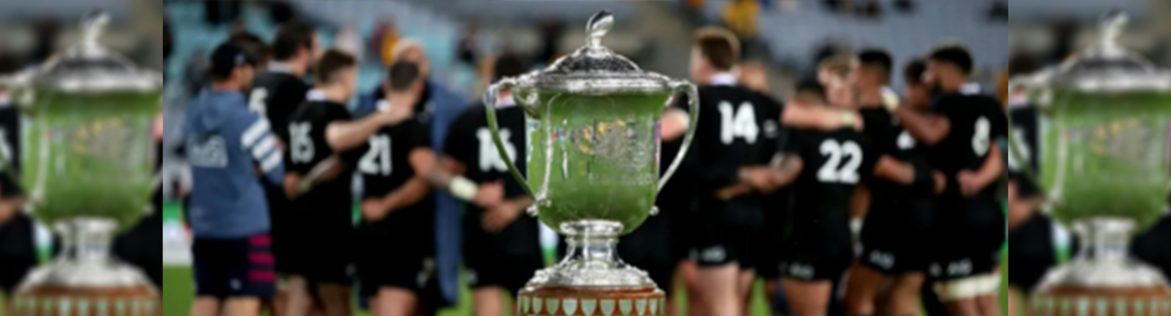 The Bledisloe Cup is in the foreground with the All Blacks in the background