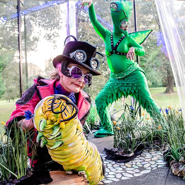Two people are dressed up in eclectic costume design to look like bugs in a greenhouse looking space