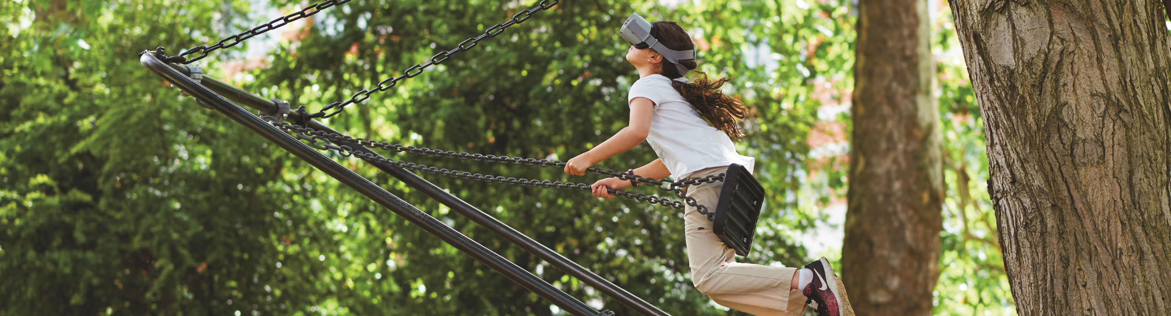 A young girl wearing a VR headset while playing on a swing