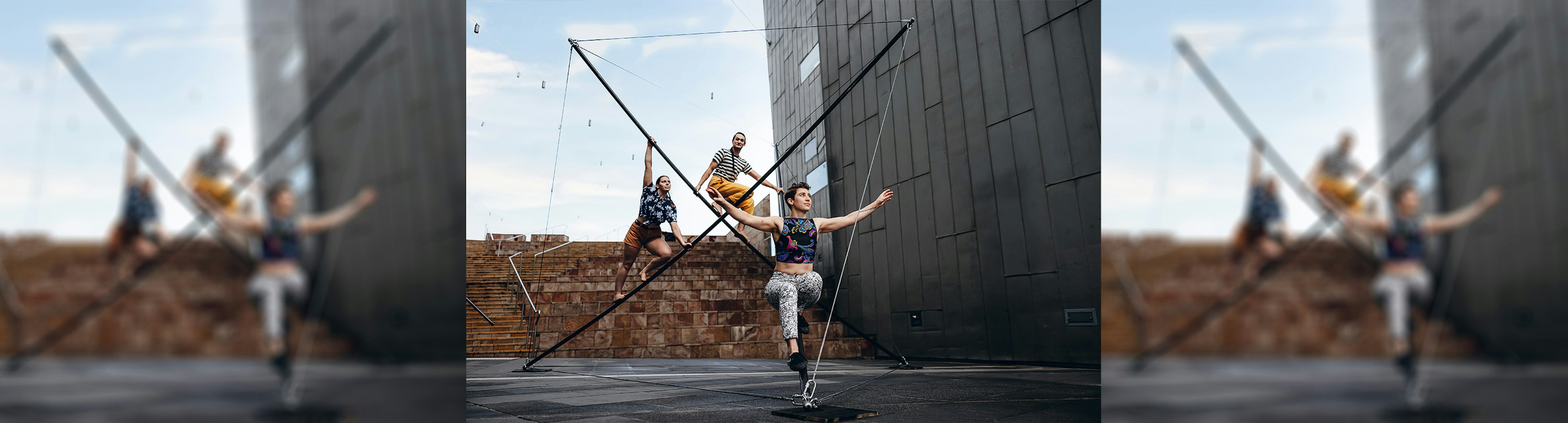 Three acrobats on a triangular shaped wire apparatus at Fed Square