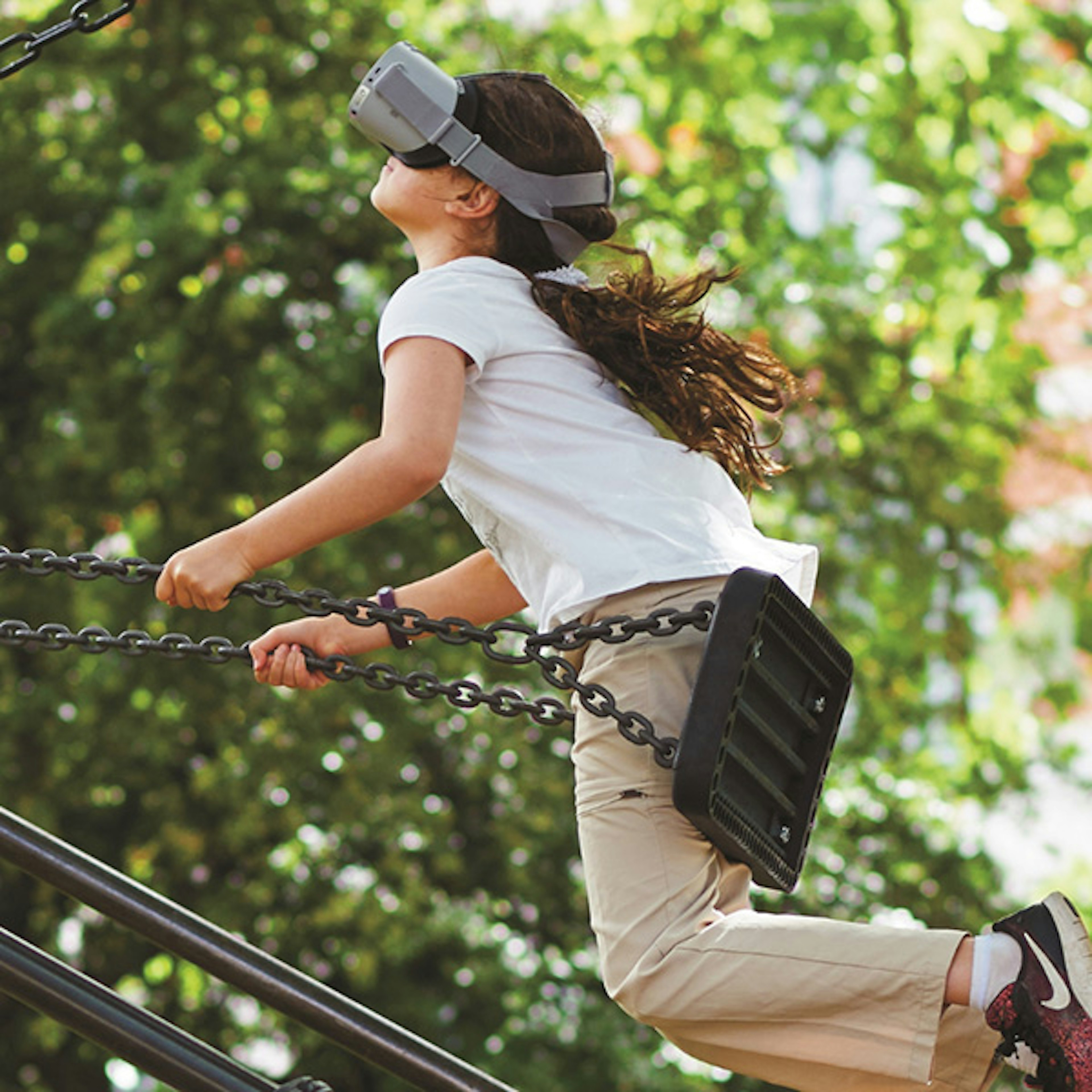 A young girl wearing a VR headset while playing on a swing