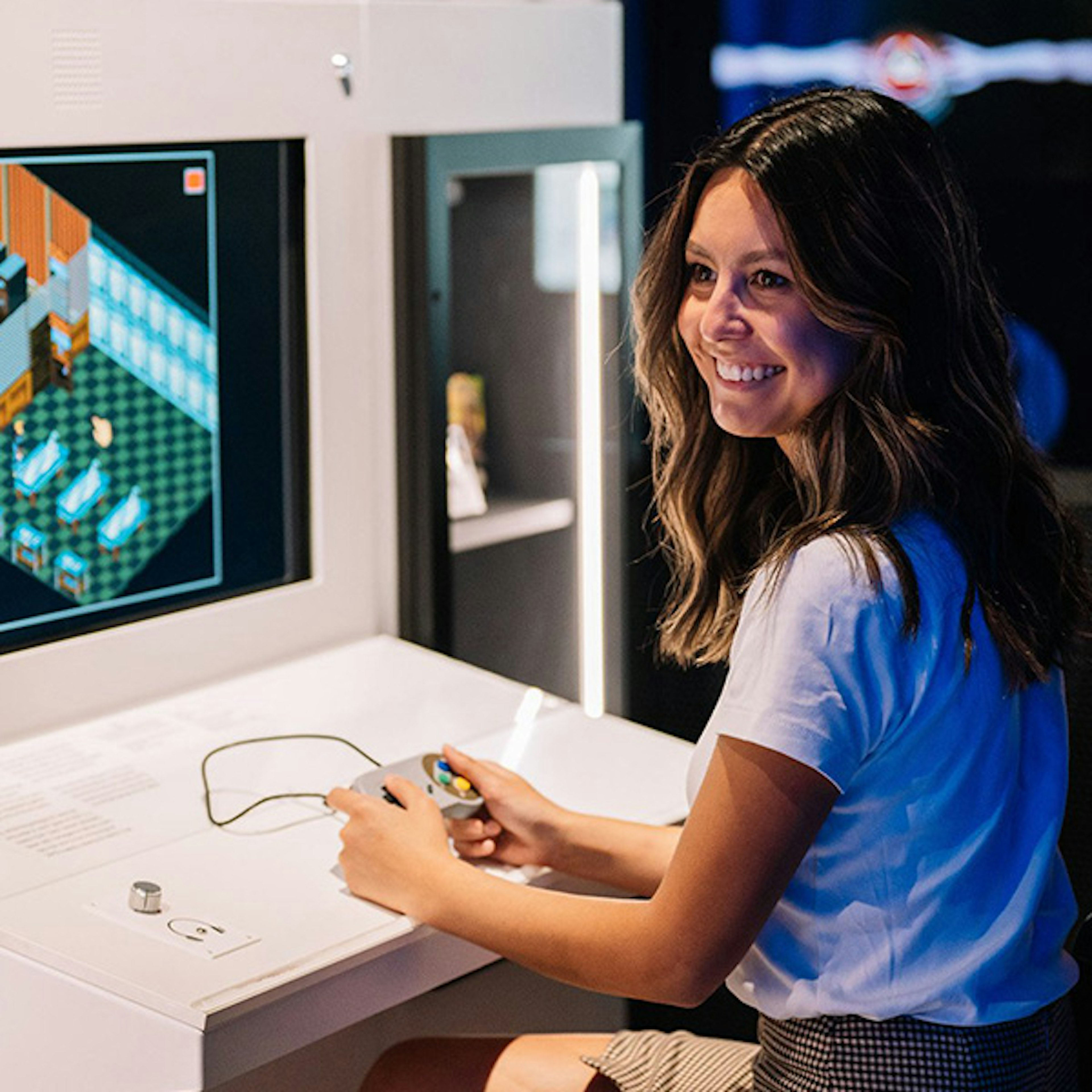 A women sitting at a console in ACMI smiling while playing an original Nintendo