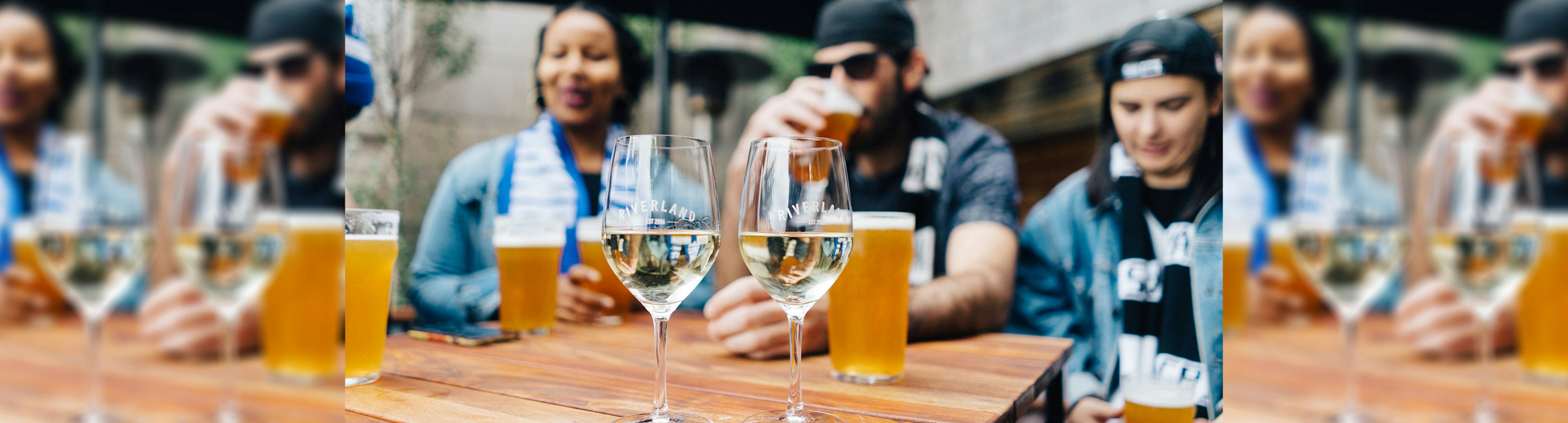 In the foreground are glasses of white wine and a pot of beer, and in the background are a group of AFL fans sitting around a table enjoying themselves