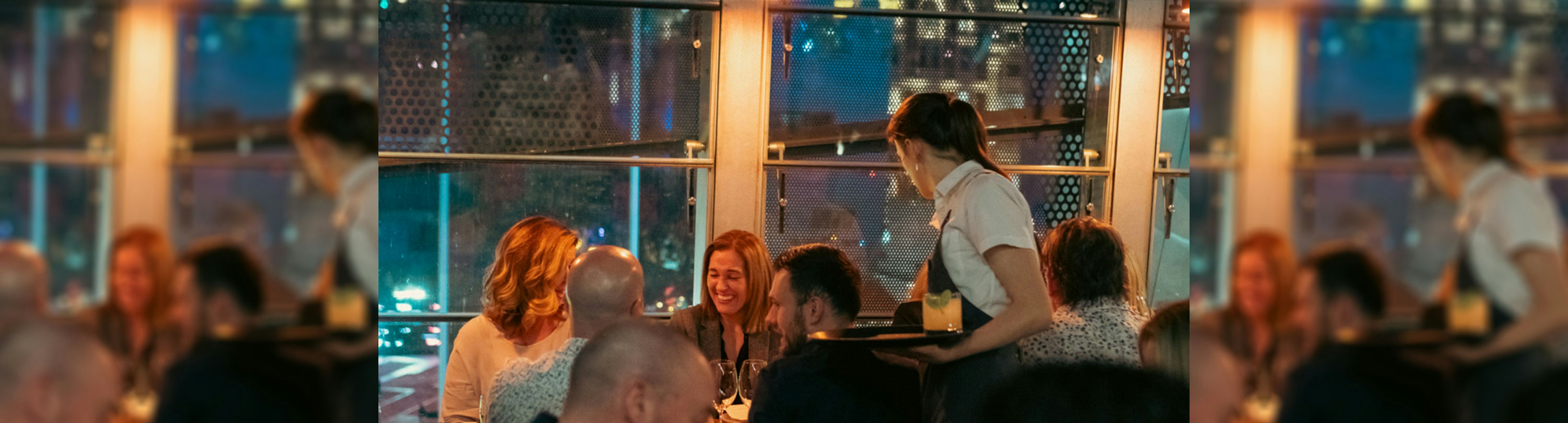 A waiter delivery drinks to smiling guests at Taxi Kitchen