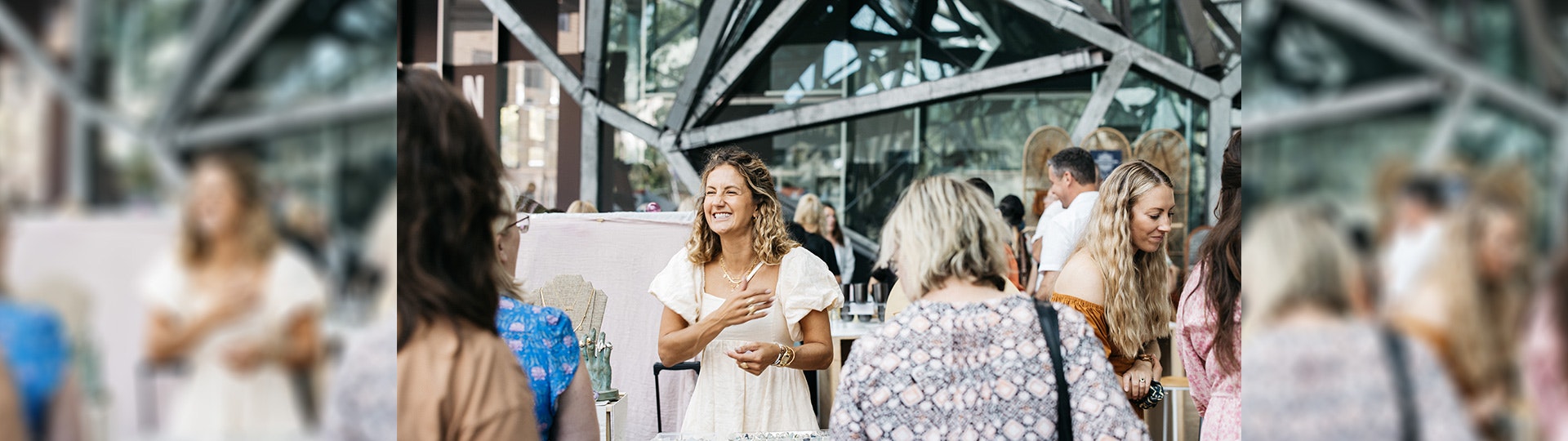 A stallholder at a market in The Atrium is grinning will speaking to a customer at their stall